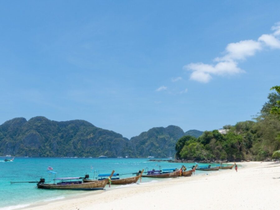 タイ・ピピ島関連ツアーで人気の美しいビーチと伝統的なロングテールボートの風景。