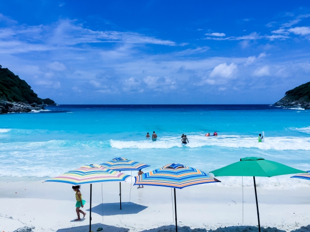 プーケットのアイランドホッピングで訪れる白い砂浜のビーチ。カラフルなパラソルが並び、波打ち際で泳ぐ人々。