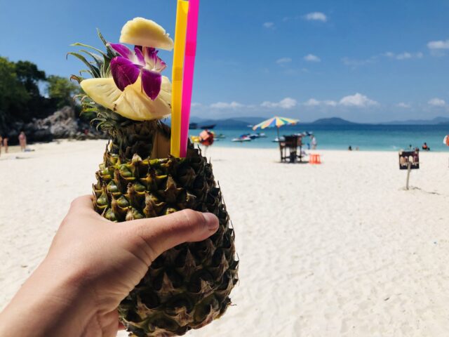 以白色沙滩和湛蓝大海为背景,手捧整颗菠萝榨出的果汁