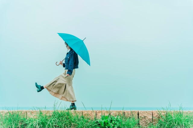 青い傘をさして海沿いを歩く女性