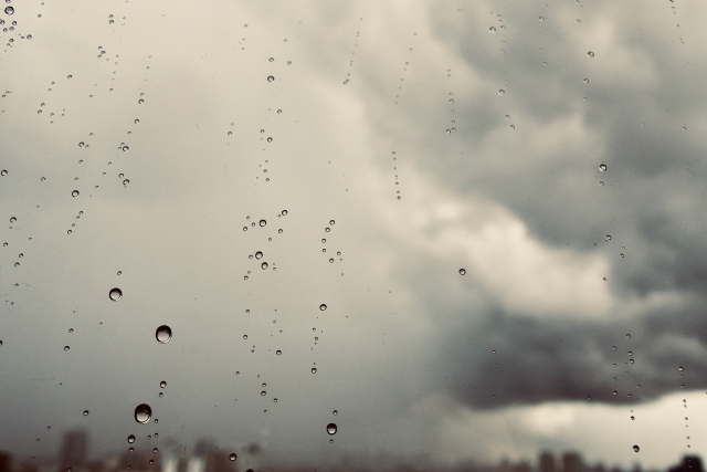 窓ガラスについた雨粒と暗い雨雲